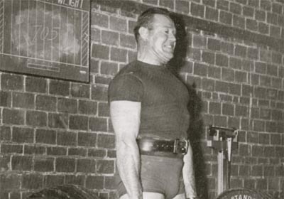 A man holding a barbell in front of a brick wall looks stronger.