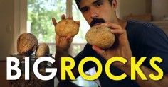In the video, a man is holding a big rock in front of a table.