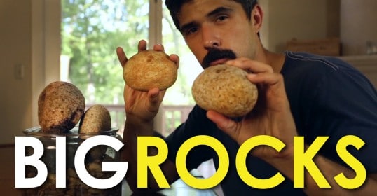 In the video, a man is holding a big rock in front of a table.