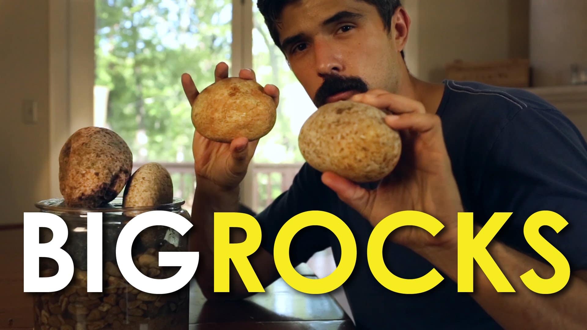 In the video, a man is holding a big rock in front of a table.