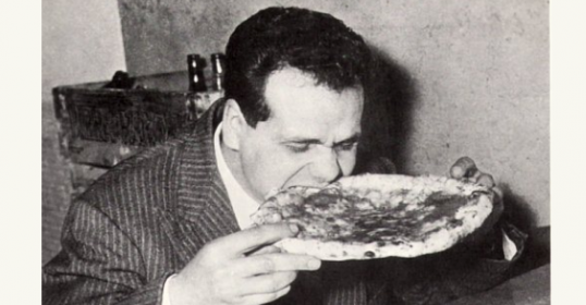 An old black and white photo of a man enjoying some pizza.