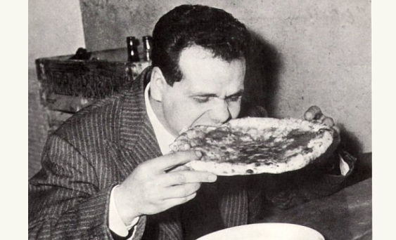 An old black and white photo of a man enjoying some pizza.