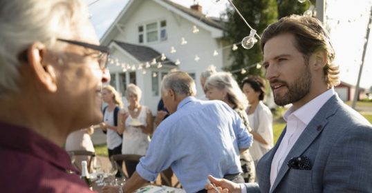 A man in a suit is holding a cake at  Meeting Someone New.