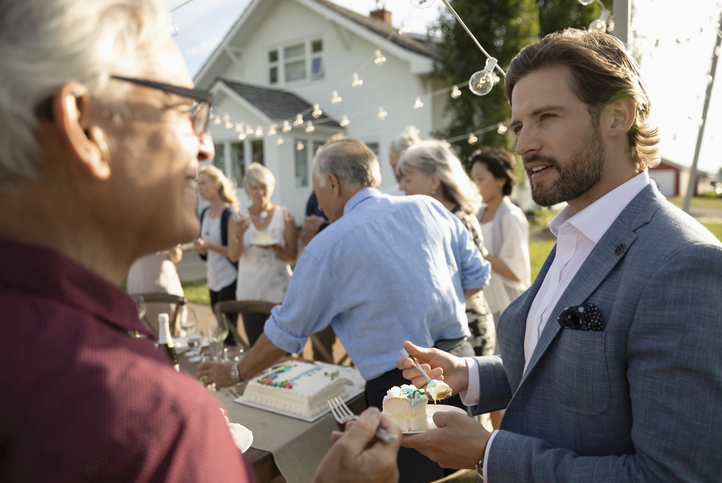 A man in a suit is holding a cake at  Meeting Someone New.