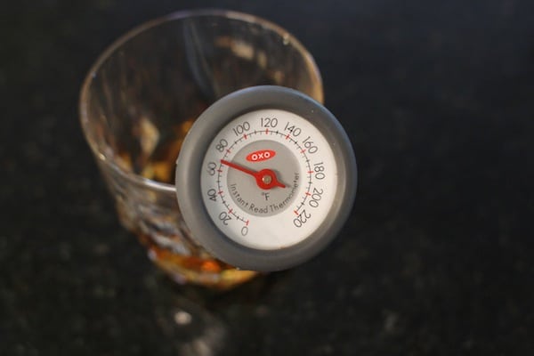 A thermometer placed in whiskey glass and measuring temperature. 