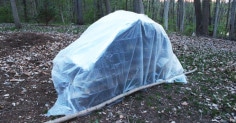 An ultimate survival shelter built in the woods, covered in plastic.