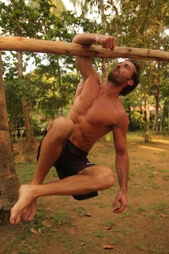 Man doing single hand pull-up on a wooden bamboo in jungle.