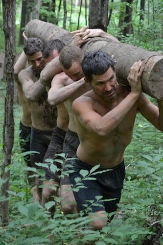 Men carrying woods log in forest. 
