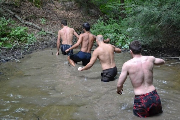 Men without shirts crossing lake in forest. 