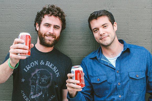 Two men standing next to each other, showcasing the art of manliness as they hold cans of Coca Cola.