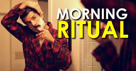 A man is shaving in front of a mirror as part of his morning routine.