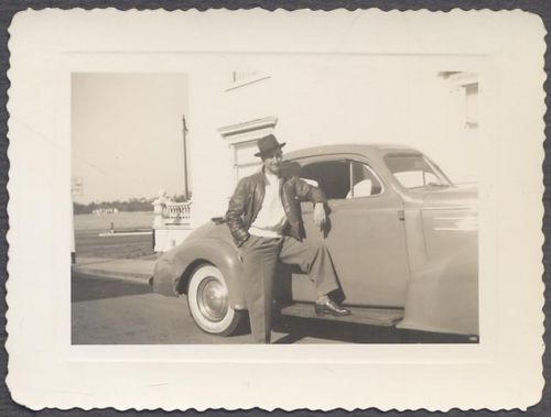 Man posing for a picture wearing leather jacket in front of car. 