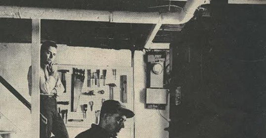 A black and white photo of two men in a room, showcasing the contrast between them.