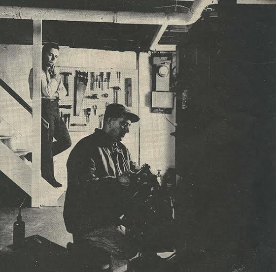 Vintage homeowner looking repairman works on furnace.