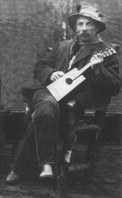 Learn how to make a cigar box guitar with this old black and white photo of a man playing an acoustic guitar.