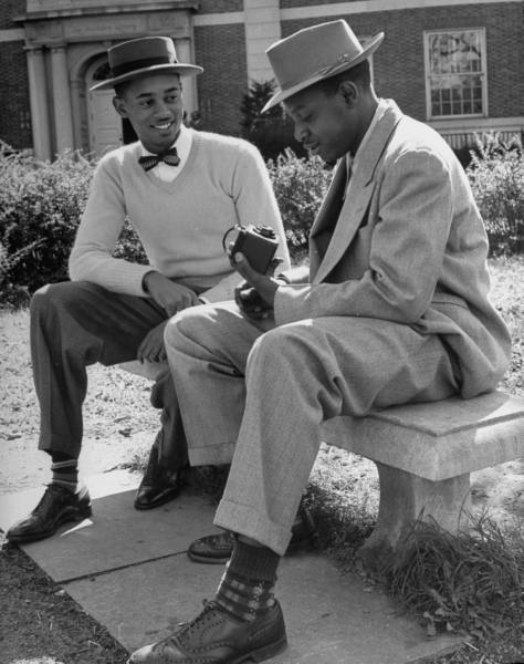 Two men in stylish hats sitting on a bench.