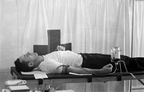 Vintage man laying on doctor table and donating blood.