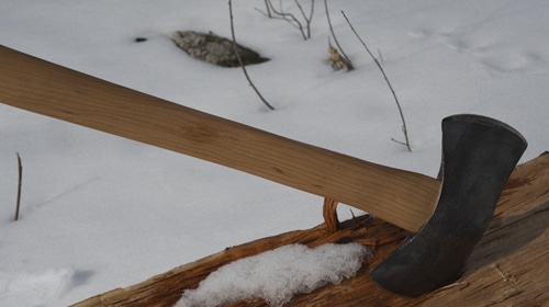 A large axe resting on a log in the snow.