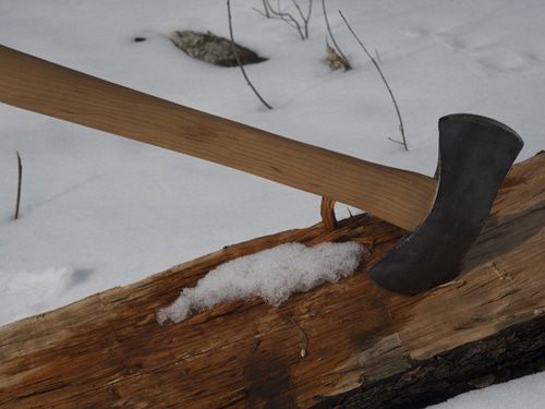 A large axe resting on a log in the snow.