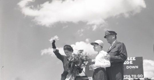 An old photo of a man and woman standing in front of a group of people, possibly from a Manvotional event.
