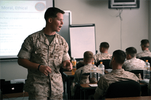 A marine in uniform is giving a presentation to a group of students, showcasing his Situational Awareness.