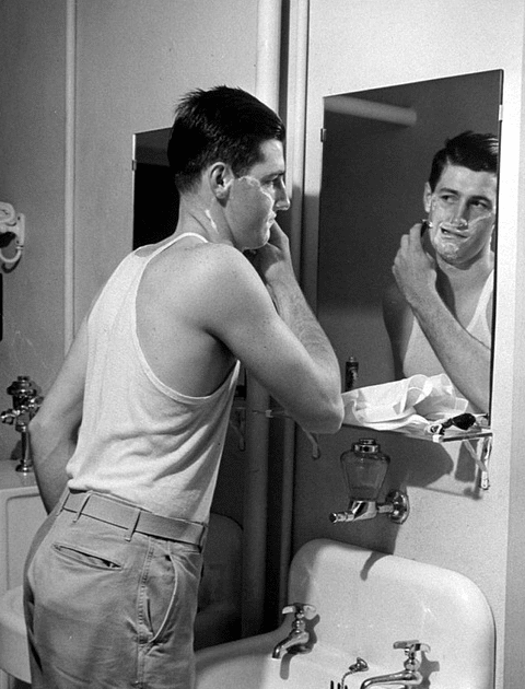 Vintage man shaving with razor and looking in mirror. 