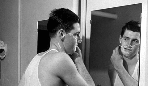 A wet shaver carefully grooming in front of a mirror.