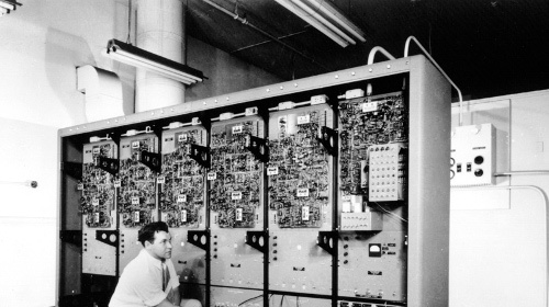 An IT professional kneeling in front of a large electronic cabinet.