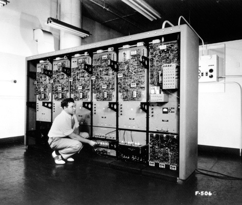 An IT professional kneeling in front of a large electronic cabinet.