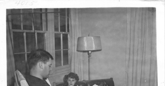 An old black and white photo of a man and woman sitting in a chair.