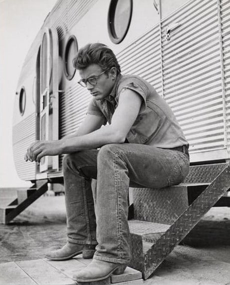 James Dean sitting outside camper wearing cowboy boots.