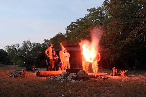 The men enjoying a signaling fire in forest. 