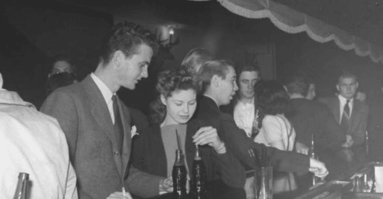 A group of shy guys standing at a bar, overcoming shyness.