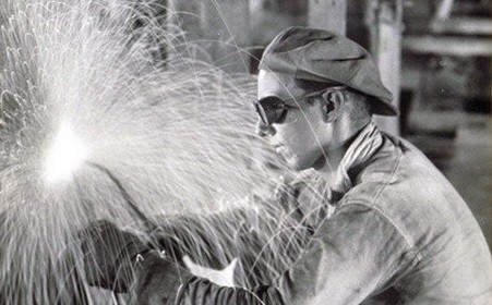 A black and white photo of a welder reviving blue collar work with sparks flying.