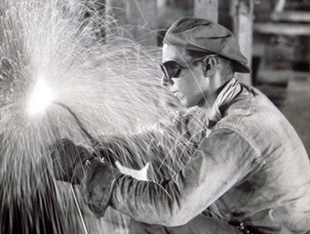 A black and white photo of a welder reviving blue collar work with sparks flying.