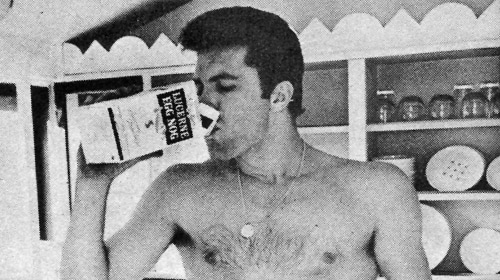 A man drinking from a bottle in the kitchen while snacking.
