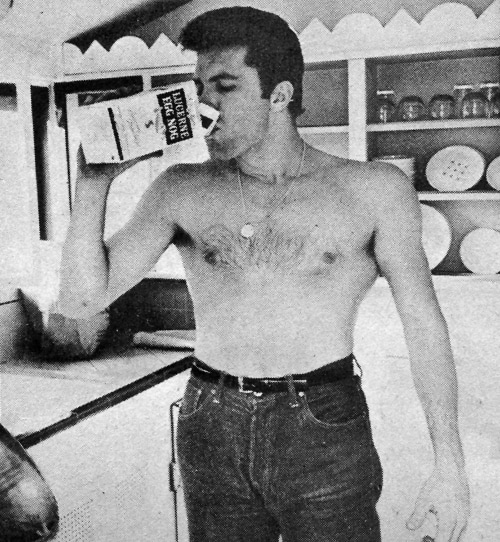 A man drinking from a bottle in the kitchen while snacking.