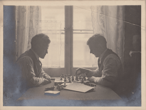 Vintge Men playing chess in front of window.