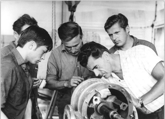 Vintage blue Collar workers working on Engine Pieces. 