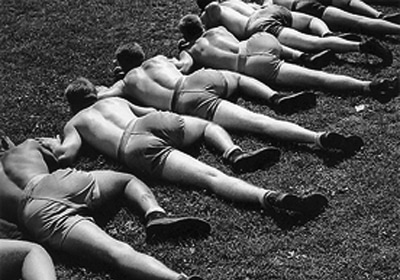 A black and white photo of a group of men doing WWII workouts on the ground.