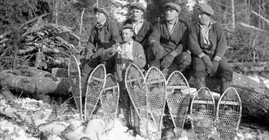 A group of men with vintage snowshoes on a log.