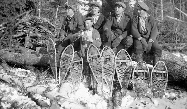 A group of men with vintage snowshoes on a log.