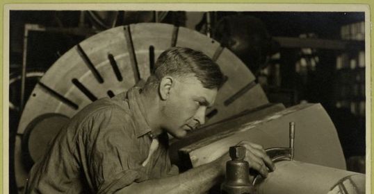 An old photo of a man working on a machine in his blue collar career.