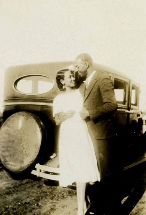 Vintage couple standing in front of car.