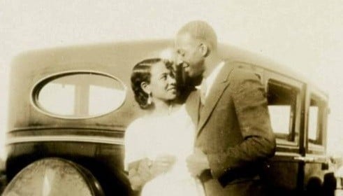 A lasting photograph of a man and woman standing next to a car.