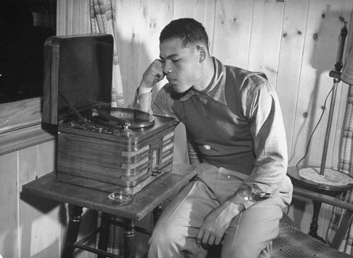 Vintage young african man listening to vinyl record player.