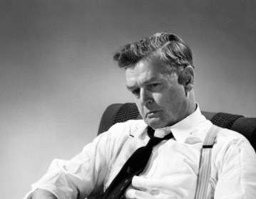 A depressed man sitting in a chair reading a book.