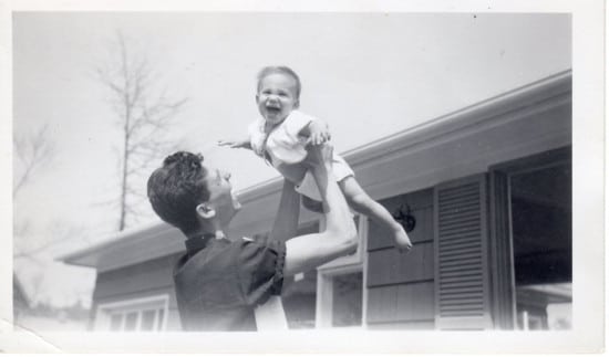 Vintage father holding son upside infront of house . 