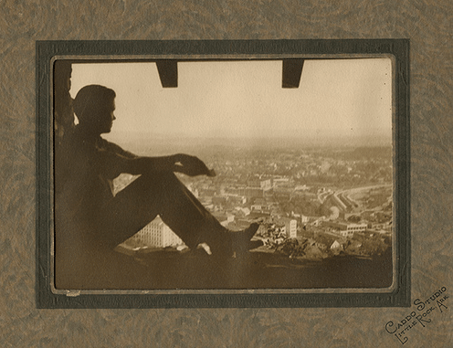 Vintage man sitting in window starting out over city. 