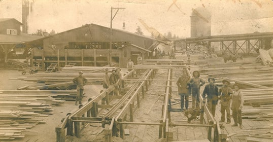A group of men standing in front of a wooden structure made of lumber.